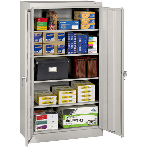 A Tennsco light gray metal storage cabinet with solid doors holding white boxes.