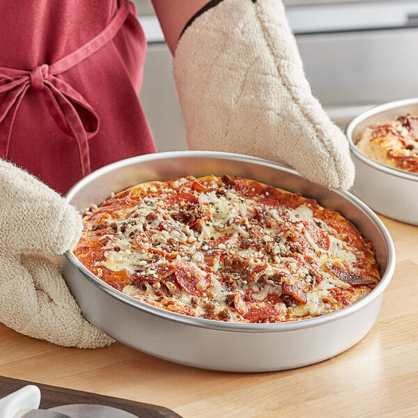 A person holding a Choice aluminum deep dish pizza pan with a pizza inside.