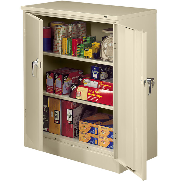 A sand Tennsco storage cabinet with solid doors full of food and other items.