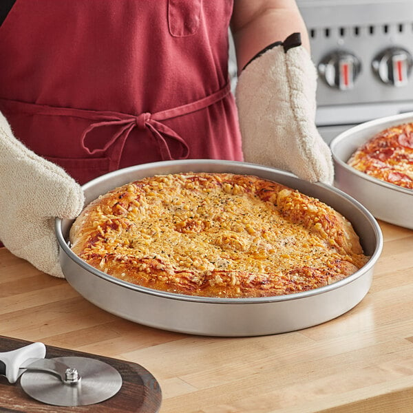 A person holding a pizza in a Choice aluminum deep dish pizza pan.