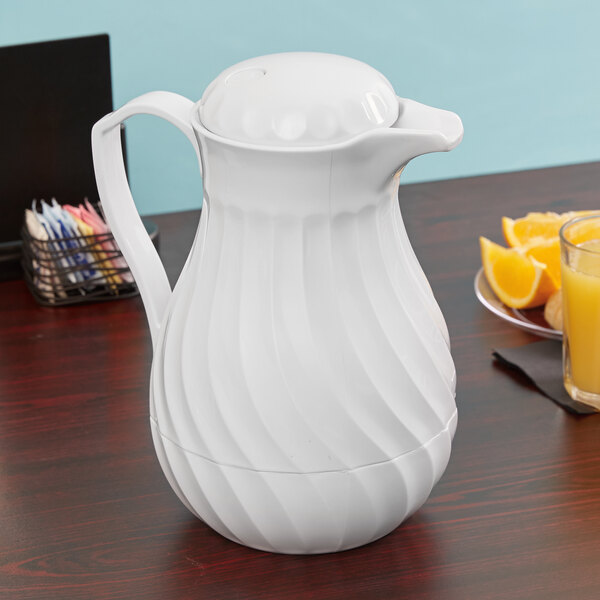 A white Vollrath beverage server on a table with a glass of orange juice and plate of oranges.