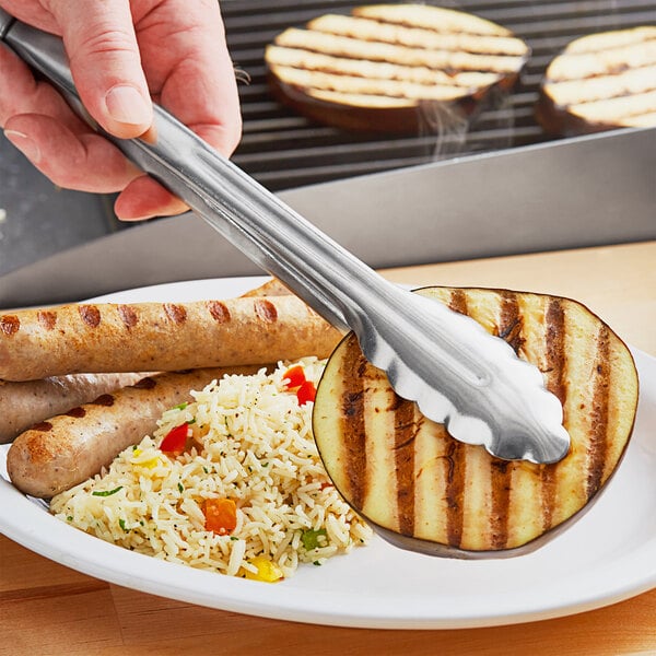 A person using Choice stainless steel utility tongs to serve food on a plate.