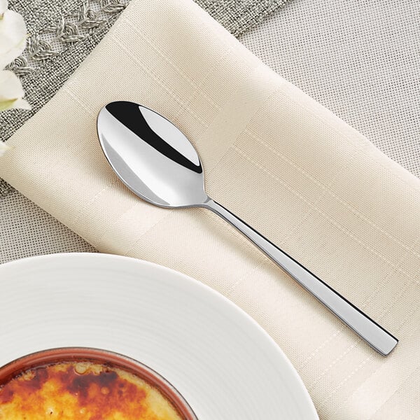 An Acopa stainless steel teaspoon on a napkin next to a plate of food.
