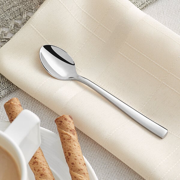 An Acopa stainless steel demitasse spoon on a napkin next to a cup of coffee.