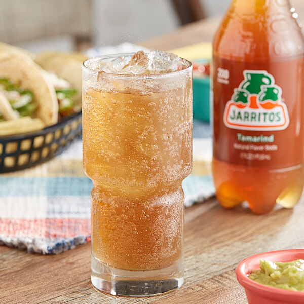 A glass of Jarritos Tamarind soda on a table with tacos and guacamole.