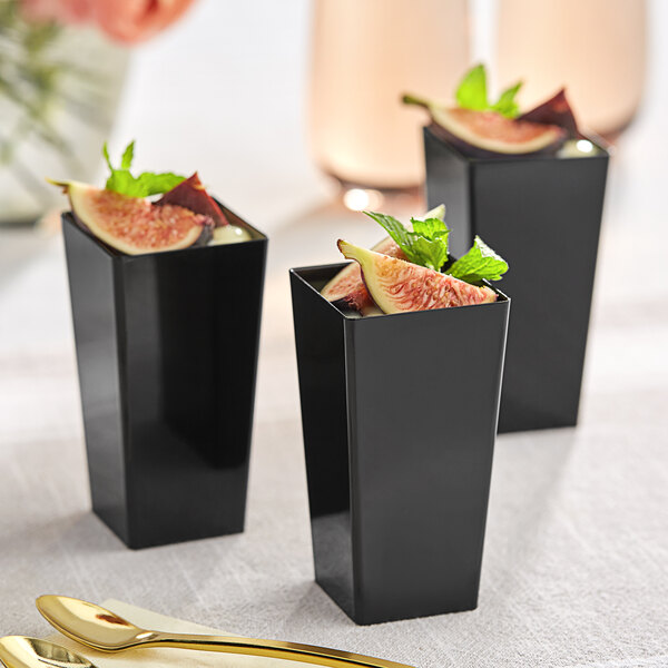 A black square plastic mini cup with a fig and mint inside.