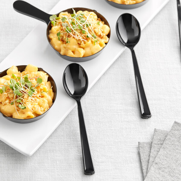 A group of black bowls of macaroni and cheese with Visions black plastic tasting spoons.