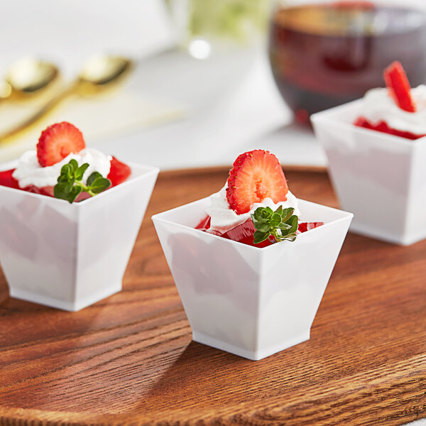 A group of small white cups filled with strawberries and whipped cream.