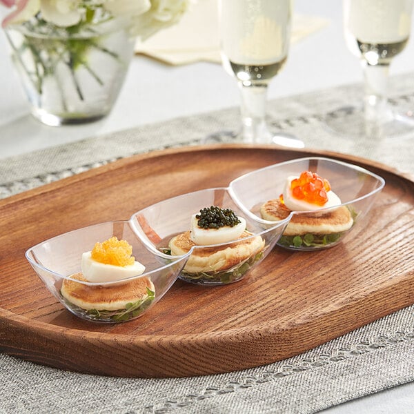 A wooden tray with three clear plastic mini bowls holding a hard boiled egg with yellow caviar.