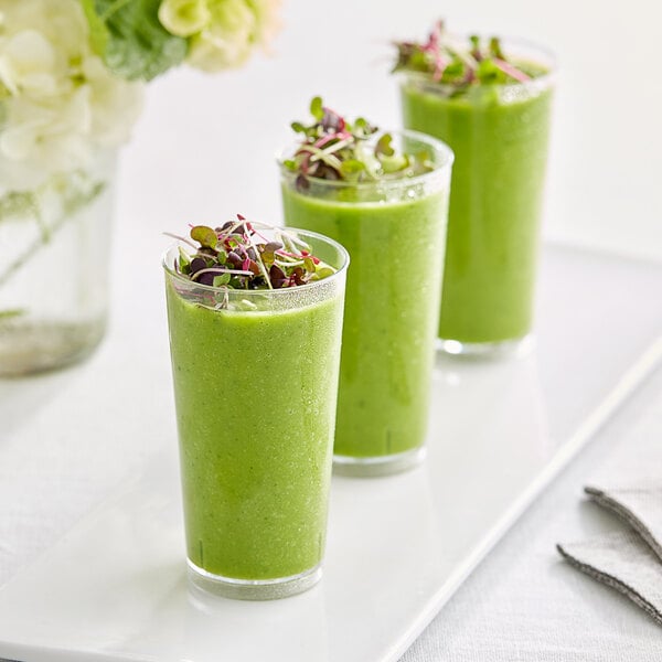 A group of green drinks in clear plastic mini cups on a white plate.
