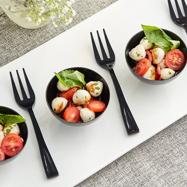 A black Visions plastic tasting fork next to a bowl of tomatoes, mozzarella, and basil.