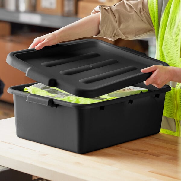A person in a yellow vest opening a black polypropylene container with a lid.