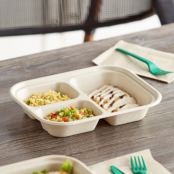 A World Centric compostable fiber container with three compartments of food on a table.