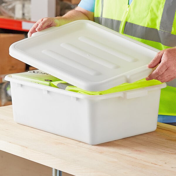 A person in a yellow vest opening a white plastic container.