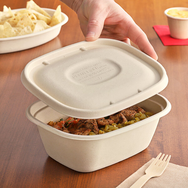 A person holding a World Centric compostable fiber lid on a container of food.
