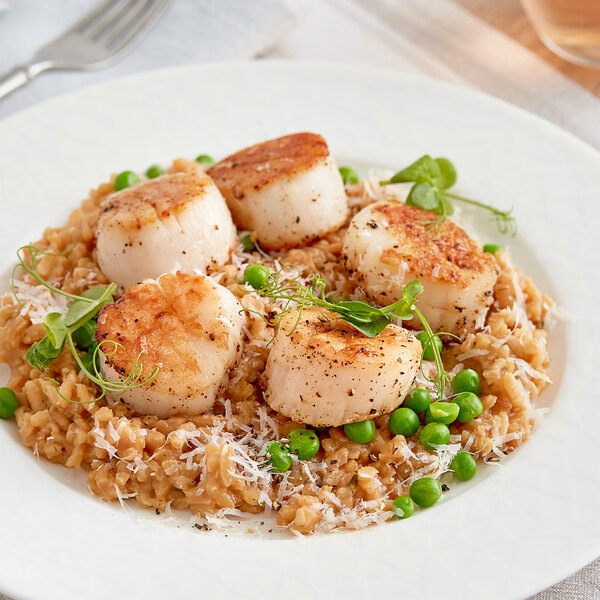 A plate of scallops and rice with peas served with Nielsen-Massey Indonesian Vanilla Extract on a table.