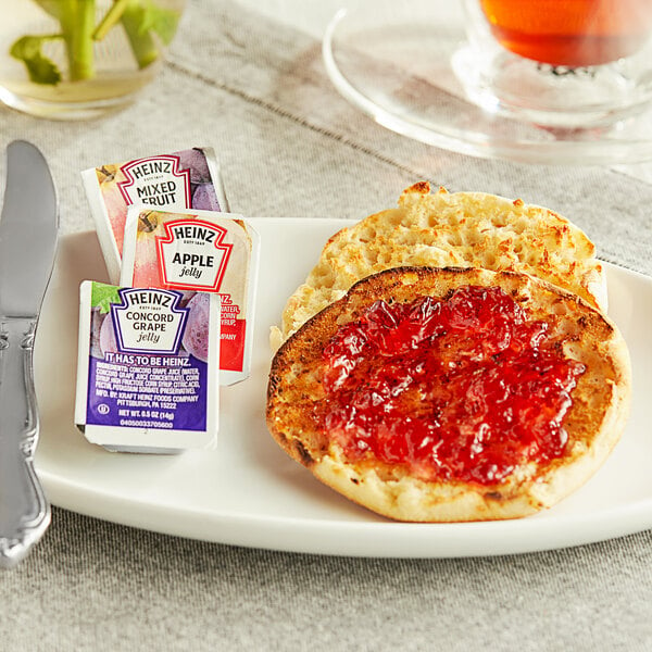 A plate with a toasted English muffin and Heinz Apple, Mixed Fruit, and Grape jelly cups on a table.