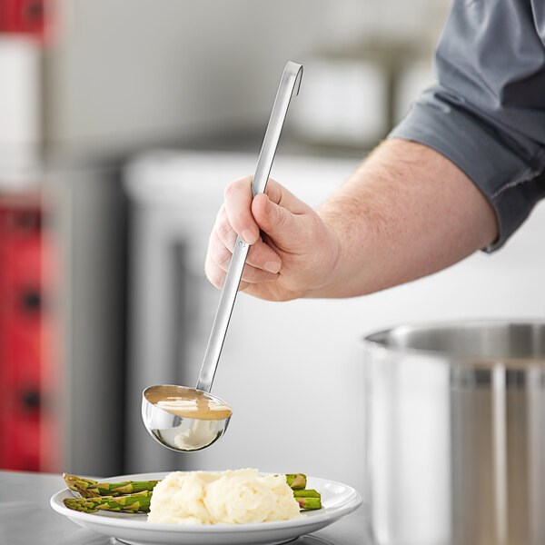 A hand holding a Choice stainless steel ladle over a plate of food.