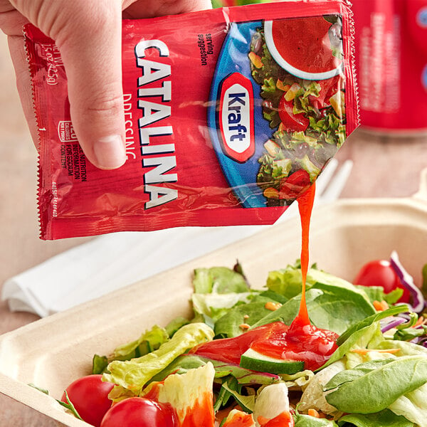 A hand pouring Kraft Catalina dressing from a red packet onto a salad.
