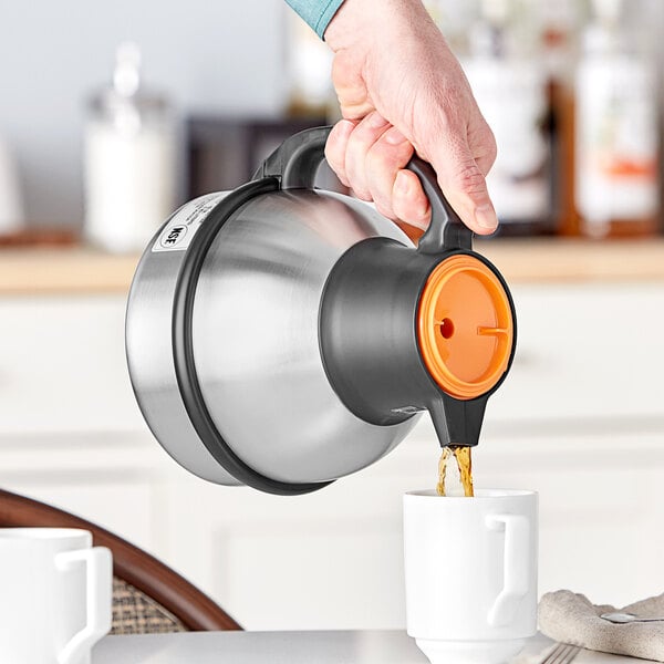 A person pouring coffee from a Bunn Zojirushi thermal carafe into a white mug.