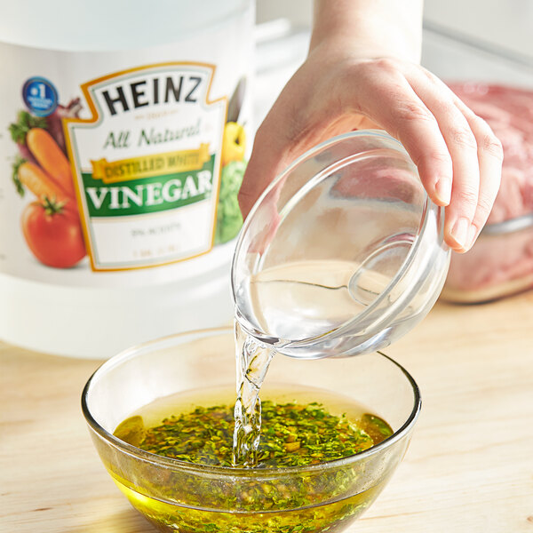 A hand pouring Heinz distilled white vinegar into a clear glass bowl.
