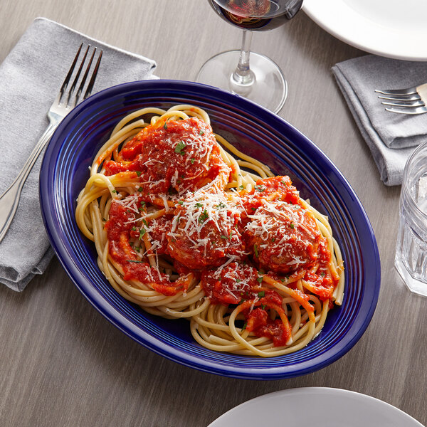 A Tuxton cobalt oval china coupe platter with a plate of spaghetti and meatballs and a fork.