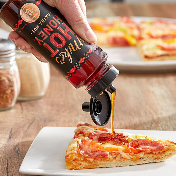 A hand pouring Mike's Hot Honey Extra Hot onto a slice of pizza.