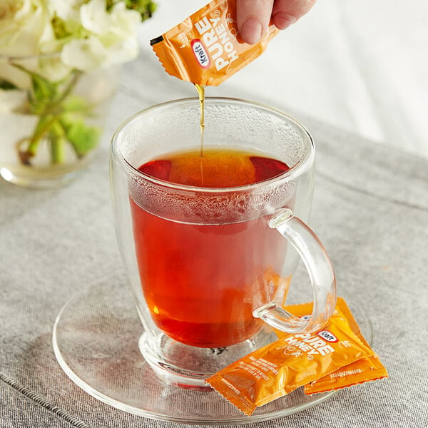 A hand pouring a Kraft Pure Honey packet into a glass of tea.