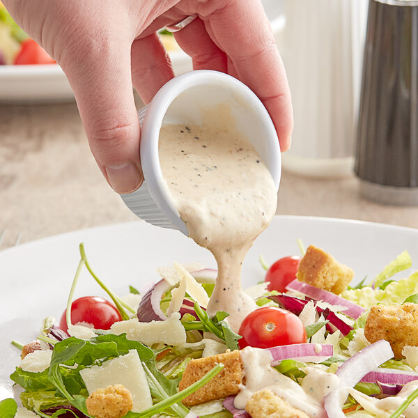 A person pouring Kraft Creamy Caesar dressing on a salad at a salad bar.