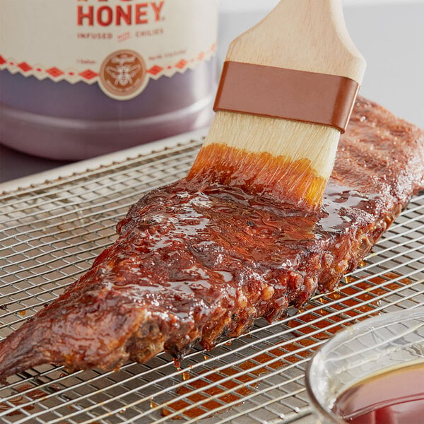 A paint brush with Mike's Hot Honey on meat on a metal grate.