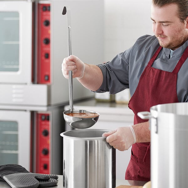 A man in a red apron using a Choice stainless steel ladle to stir a pot.