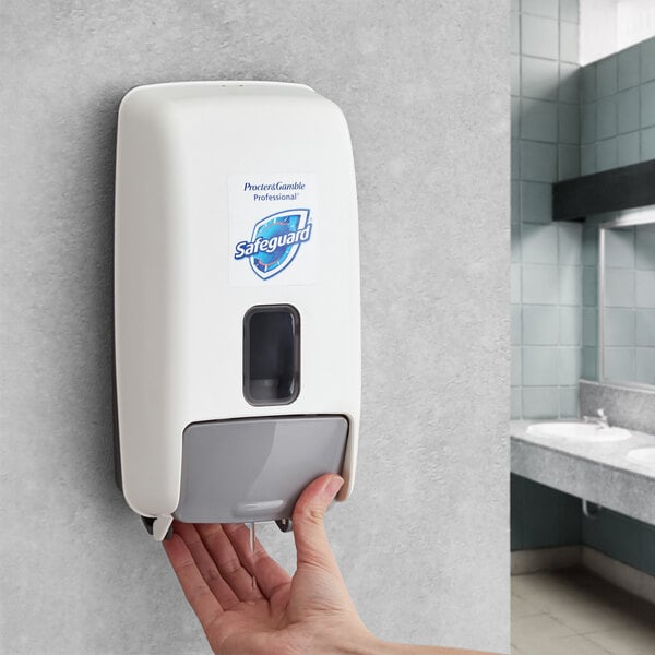 A hand pressing a button on a Safeguard Professional manual hand sanitizer dispenser on a wall.