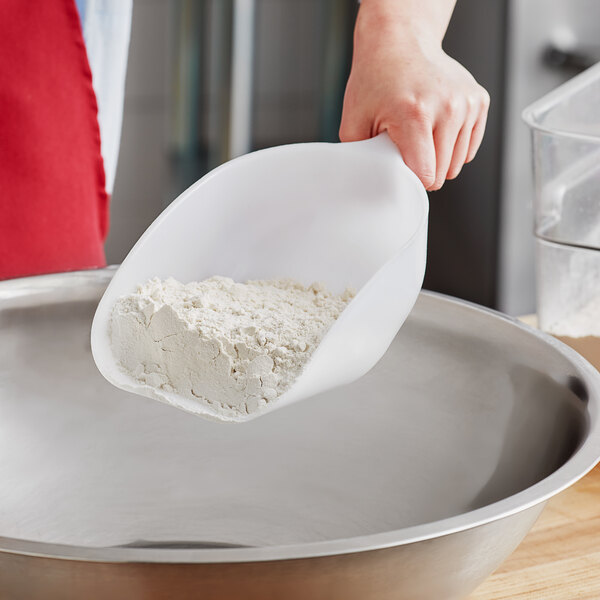 A person using a Choice white plastic round bottom scoop to pour flour into a bowl.