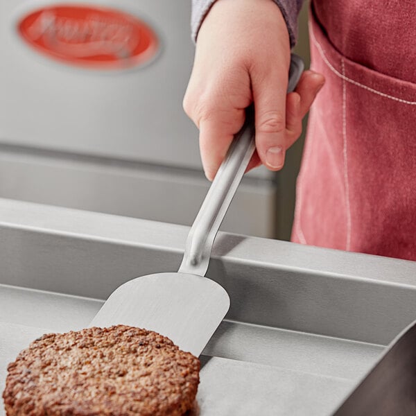 A hand holding a Choice stainless steel spatula over a burger patty.