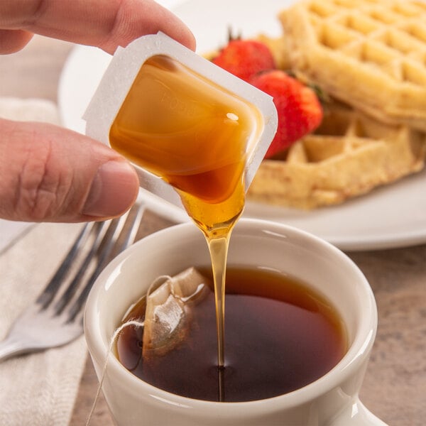 A person pouring honey into a cup of tea.