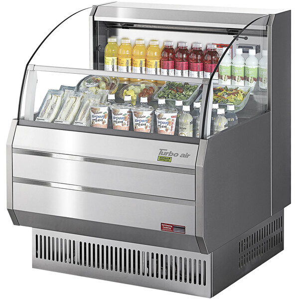 A Turbo Air stainless steel slim line horizontal air curtain display case on a counter with drinks and snacks inside.