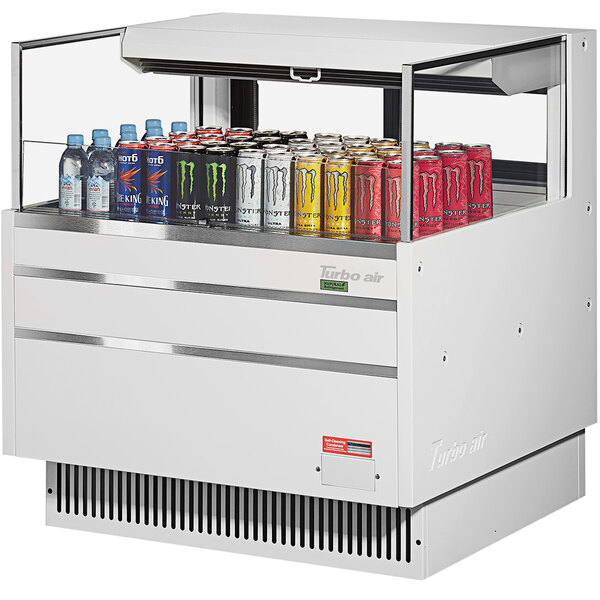 A white Turbo Air refrigerated curtain merchandiser filled with soda and cans of different colors.