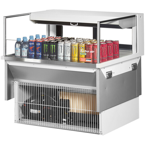A Turbo Air white drop-in refrigerated display case with cans of soda and energy drinks.