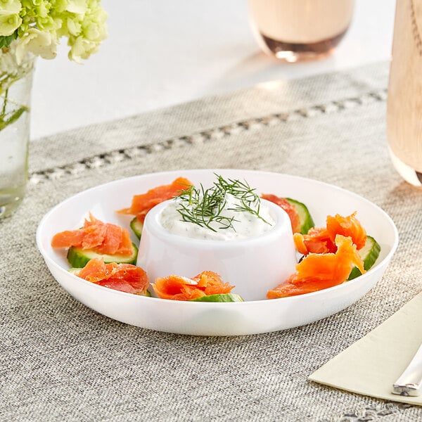 A white plastic circular dip tray with a white bowl of cream with green sprigs on top on a table.