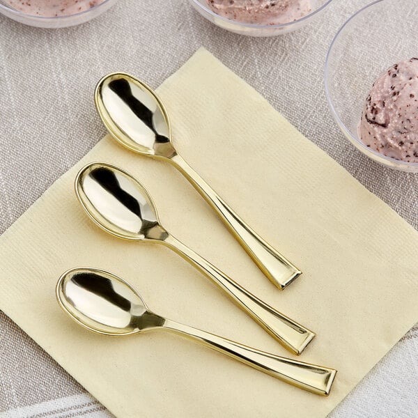 A close up of a Visions gold plastic tasting spoon on a napkin next to bowls of ice cream.