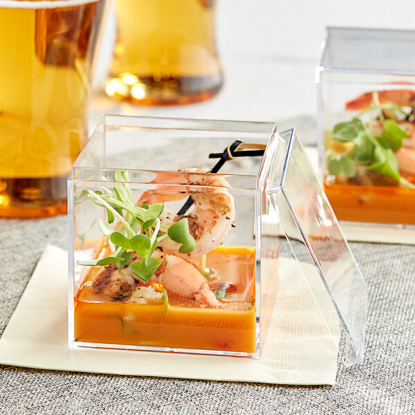 A Visions clear plastic mini cube with shrimp inside on a table at a catering event.