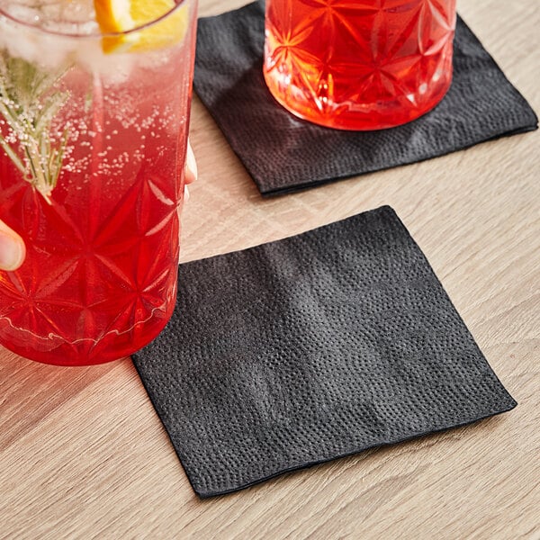 A hand holding a glass of red liquid with a lemon and a black Choice beverage napkin on a table.