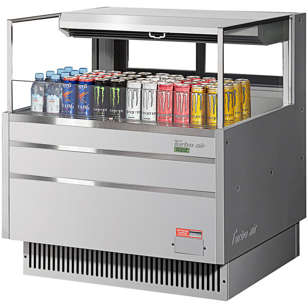 A Turbo Air stainless steel horizontal refrigerated cooler filled with soda cans of different colors.