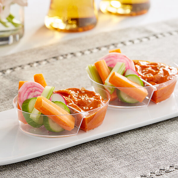 A Choice clear plastic mini dual compartment dish with vegetables and dip in each compartment.