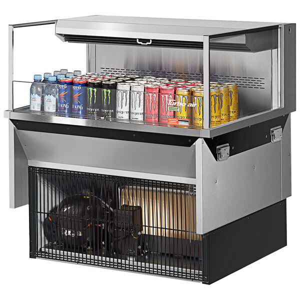A Turbo Air refrigerated open display case with cans of soda on a counter.