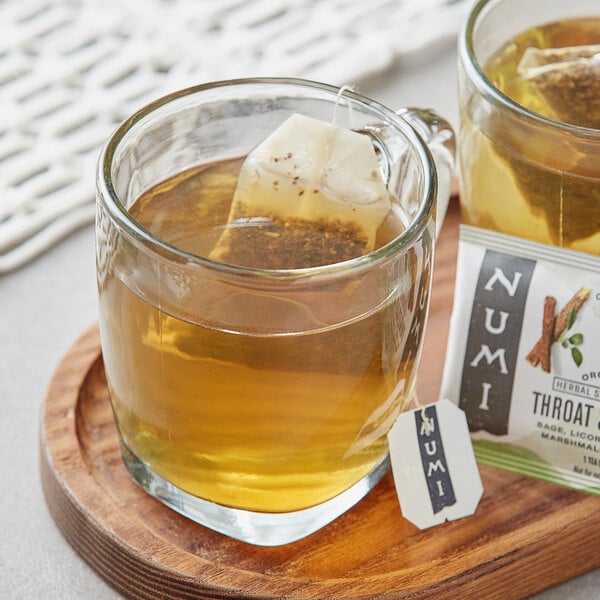 A glass mug of Numi Organic Throat Soother tea with a tea bag in it.
