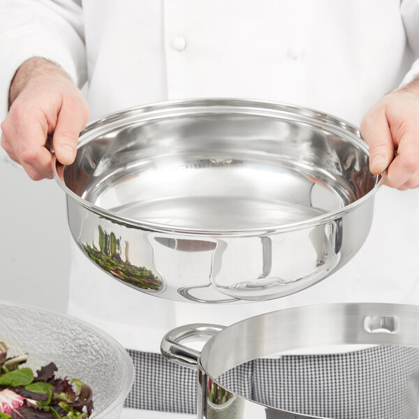 A chef holding a stainless steel water pan.