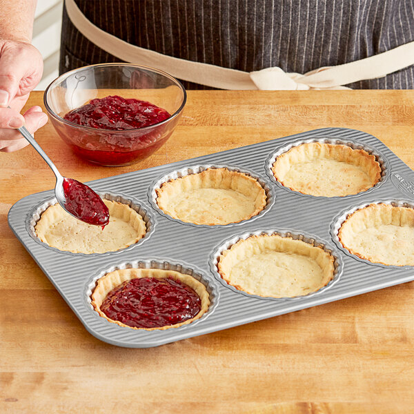 A person using a Chicago Metallic silicone fluted tart pan to make tarts and fill the cavities with jam.