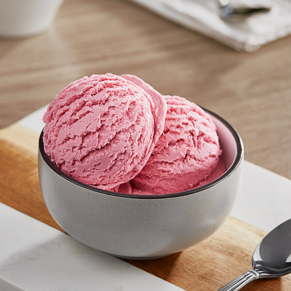 A bowl of pink ice cream with a spoon on a white surface.