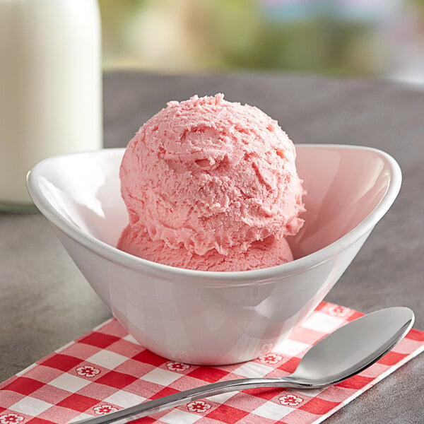 A bowl of pink ice cream with Oringer Seedless Strawberry Puree Hard Serve Ice Cream Base on a table with a spoon.